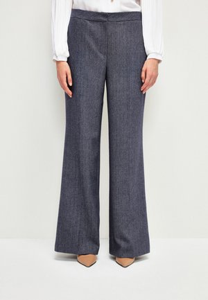 Pantaloni a gamba larga in un motivo herringbone blu navy, realizzati in tessuto testurizzato. Presentano una vita liscia e sono abbinati a scarpe beige a punta.