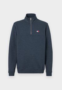 Sweatshirt azul marinho com um colarinho alto, fecho de meio zíper na parte da frente e punhos elásticos. Apresenta um pequeno emblema no lado superior esquerdo do peito. Textura suave.
