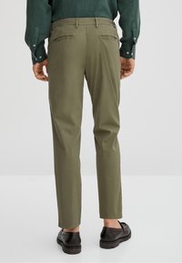 Oliwkowe chinosy o prostym kroju, z dwiema tylnymi kieszeniami i gładką fakturą, w połączeniu z czarnymi butami.