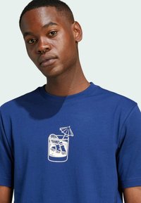 T-shirt in cotone blu con grafica bianca di una bevanda in un bicchiere con ghiaccio e una piccola ombrellino. Collo rotondo, maniche corte.