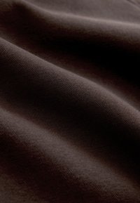 Sötétbarna puha szövet jól látható finom textúrával és lágy redőkkel, amelyek árnyékokat és fényeket hoznak létre a felületen.