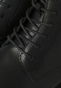 Botas de tobillo de cuero negro con un intrincado sistema de cordones, parte superior texturizada y sutiles detalles de costura. Acabado suave con una silueta elegante.