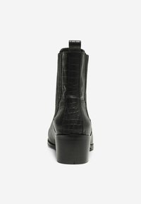Botín de cuero negro hasta el tobillo con un patrón de cocodrilo, punta redonda y un tacón bajo en bloque. Cuenta con una lengüeta para facilitar el uso.