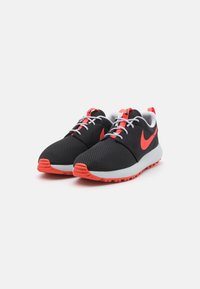 Sapatilhas Nike com um upper em malha preta, detalhes em vermelho brilhante, atacadores brancos e uma sola de borracha branca com uma textura de tração.
