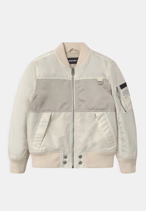 Beige bomberjakke med en lysebrun horisontal panel, ribstrikkede manchetter, to sidelommer og sidelomme med lynlåsdetalje.