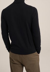 Mörkblå polotröja i slät stickad tyg. Figursydd design med ribbade muddar och fåll, bärs med ljusbruna byxor.