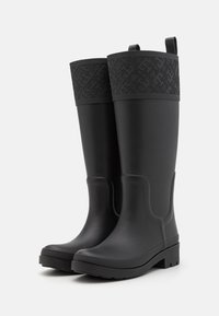 Bottes de pluie en caoutchouc noir avec une tige supérieure texturée et imprimée, semelle plate et languettes pour un enfilage facile. Conçues pour résister à l'eau.