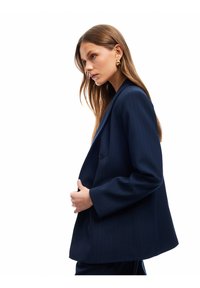 Sinih raja garis blazer dengan penutupan double-button, lapel lebar, dan fit sedikit besar. Kain halus dengan desain terstruktur.