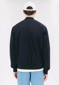 Zwarte bomberjack met een gladde textuur, geribde manchetten en zoom; heeft een strak ontwerp zonder zichtbare versieringen, getoond vanaf de achterkant.