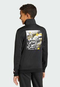 Musta fleecepusero, jossa on korkea kaulus ja selässä graafinen printti keltaisin korostuksin. Sileä pinta, rento istuvuus.