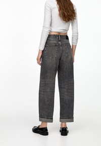 Jean en denim gris taille haute et coupe ample avec texture délavée. Comprend cinq poches et des revers retroussés. Porté avec un haut léger à manches longues.