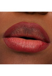 Matowa burgundowa szminka na pełnych ustach o gładkiej fakturze, z subtelnymi gradientami od ciemniejszych do jaśniejszych odcieni w kierunku środka.