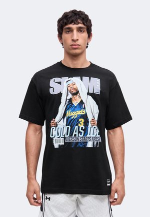 Jeune homme porte un t-shirt noir avec un graphisme du joueur de basket Allen Iverson en maillot des Nuggets et texte "Slam," "Cold As Ice," et "Iverson Starts Fresh."