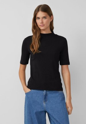 Zwart kortemouwen top met een opstaande kraag, gemaakt van een gladde stof. Strakke pasvorm, aangevuld met blauwe wijde denim jeans. Minimalistische stijl.