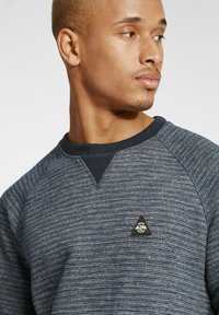 Tengerészeti crew neck pulóver texturált, mintás anyagból, bord�ázott nyakkal és egy kis, háromszög alakú logópászma a mellkason.