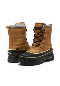 Bruna vinterstövlar i läder med grå pälsfoder, svart gummitätning vid tån, guldfärgade metallbeslag och tjock sula med mönster och logotypdetalj.