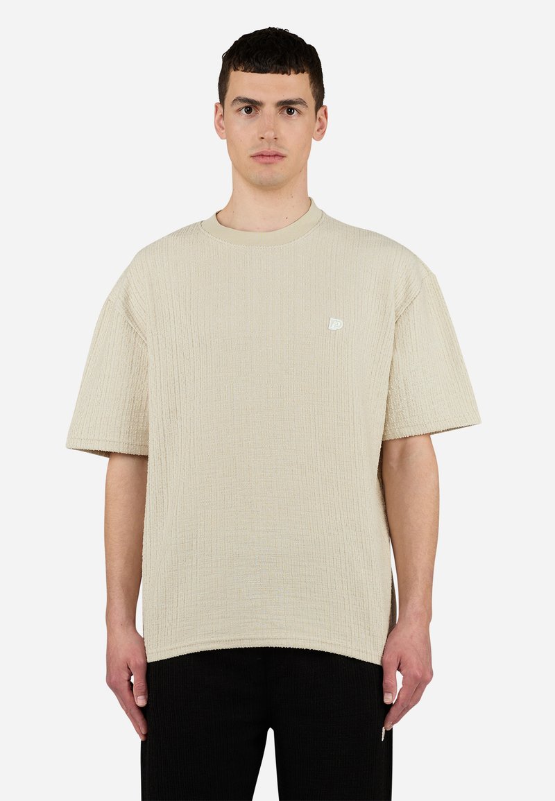 T-shirt beige texturé en tissu côtelé. Il présente un col rond et des manches courtes. Petite étiquette logo sur la poitrine.
