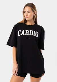 Svart oversized t-shirt i bomull, med fet vit text "CARDIO" på framsidan, kort ärm och rund halsringning.