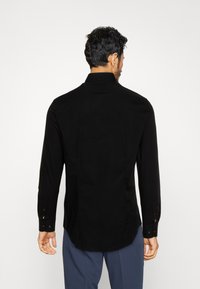 Schwarzes Langarmhemd mit taillierter Passform, das einen klassischen Kragen und knöpfbare Manschetten aufweist. Glattes Material mit einem klaren, minimalistischen Design.