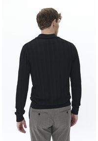 Suéter negro de punto con un diseño de canalé texturizado, con cuello y mangas largas, combinado con pantalones grises a rayas.