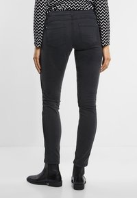 Hubené černé džíny s hladkou texturou, vybavené zadními kapsami a bočním švem. Spárováno s kotníkovými botami.