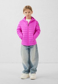 Roze donsjack met capuchon, ritssluiting en horizontaal doorgestikt patroon. Gecombineerd met lichtblauwe wijde spijkerbroek en witte sneakers.