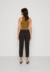 Fekete, magas derekú farmert viselő, taperszárú nadrág, figyelmesen párosítva egy illeszkedő, olíva zöld crop toppal. Az alakítás sima textúrájú és minimalista dizájnú.