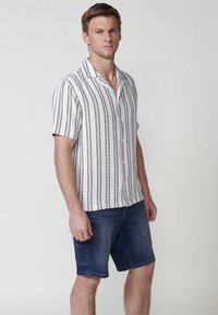Rövid ujjú, galléros ing, függőleges fekete-fehér csíkokkal, farmer rövidnadrággal párosítva. Az ing laza szabású és gombos záródású.