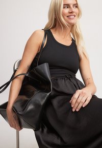 Črna usnjena torba s strukturiranim, zloženim dizajnom. Torba ima dvojni naramnici, dopolnjena z gladko, svetlečo teksturo.