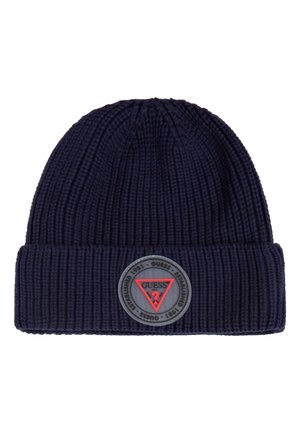 Navy blue ribbed knit beanie with folded cuff featuring a round Guess logo patch with red triangle and text on front.