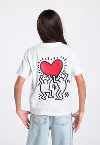 Wit katoenen t-shirt met een grafisch ontwerp op de achterkant, bestaande uit een groot rood hart en twee abstracte figuren in zwarte lijntekeningen.