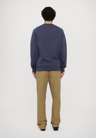 Marineblå sweatshirt med rund hals og raglanærmer, matchet med beige bukser. Stoffet ser mykt ut med en ensfarget overflate.