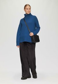 Blauwe coltrui met ribbelstructuur, gecombineerd met zwarte wijde broek en een kleine gestructureerde zwarte tas, gedragen met stevige zwarte schoenen.