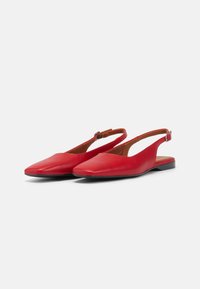 Chaussures slingback en cuir rouge avec un bout pointu, des côtés ouverts et une semelle noire basse. Comprend une sangle réglable au niveau du talon.
