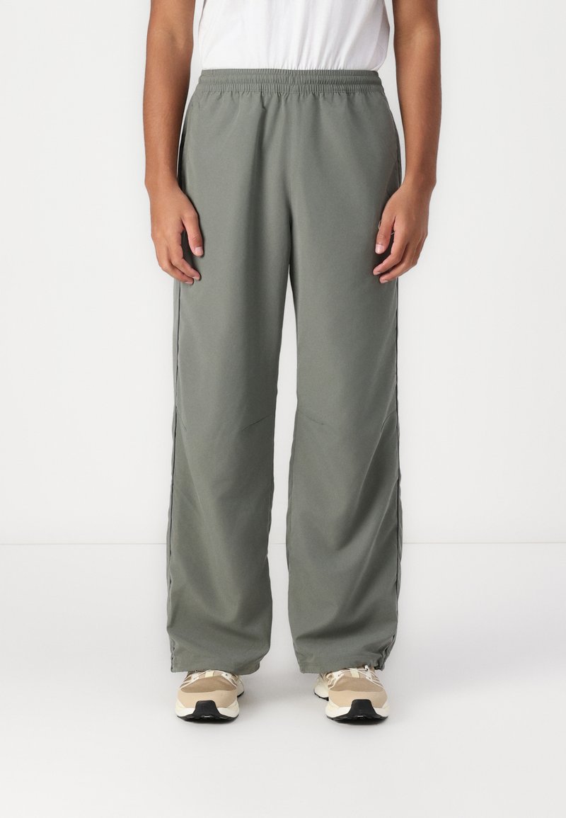 Grønne sweatpants med løs pasform, elastisk talje, sidelommer og en glat tekstur, parret med beige træningssko.