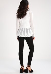 Vit stickad tröja med ett texturerat mönster och scalloped nederkant, ihop med svarta leggings och svarta blockklacksandaler.