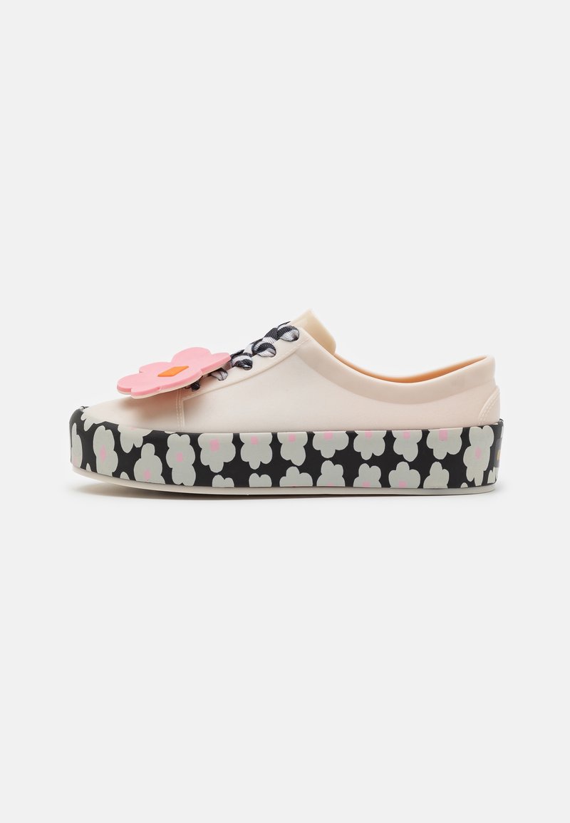 Baskets basses crème avec semelle à motif floral noir et blanc et grand accessoire fleur rose sur le dessus près des lacets.
