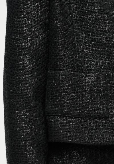 Čierna textúrovaná látka blazra s tkaným vzorom, jedným vreckom a mierne lesklým povrchom.