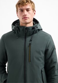 Groene hooded jas met een ritssluiting aan de voorkant, zijzakken en verstelbare trekkoorden. Heeft een subtiele textuur en contrasterende ritsdetails.