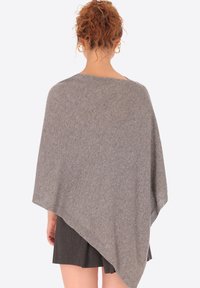 Poncho grigio realizzato in un morbido tessuto strutturato. Presenta una forma ampia e drappeggiata con un colletto ampio e lati aperti, in contrasto con una gonna scura.