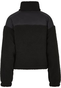 Černá fleecová bunda s vysokým límcem, měkkou texturou a kontrastní hladkou černou horní částí. Zkrácený střih s pokleslými rameny.