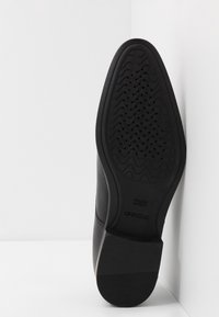 Semelle de chaussure en cuir noir présentant un motif texturé avec des motifs en zigzag, des trous de ventilation et un talon empilé. Marquée "GEOX" et "BREVET ITALIEN."