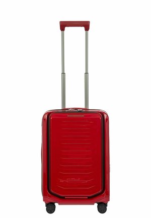 Valigia rigida rossa con finitura liscia, scanalature orizzontali, maniglia telescopica e quattro ruote per la manovrabilità.
