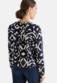 Marineblauwe blouse met geometrische beige patronen, lange mouwen en een relaxed fit. Heeft een ronde halslijn en een zachte stoftextuur.