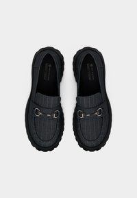 Mocassins en tissu gris à motif rayé, semelles en caoutchouc noir et détails en métal argenté sur l'avant. Finition en matériau texturé.