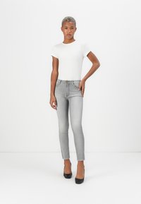 Grå tettsittende jeans med slank silhuett og frayed ankelkanter, kombinert med en hvit kortermet topp og svarte høye hæler.