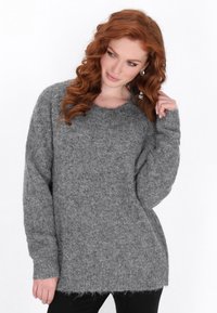 Grauer Strickpullover mit lockerer Passform, weiten Ärmeln, gerippten Bündchen und einem leicht ausgefransten Saum. Weiches, strukturiertes Wollmaterial.