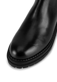 Czarne skórzane botki za kostkę o gładkiej powierzchni, zaokrąglonym czubku, teksturowanej podeszwie oraz dekoracyjnym przeszyciu wzdłuż krawędzi podeszwy.