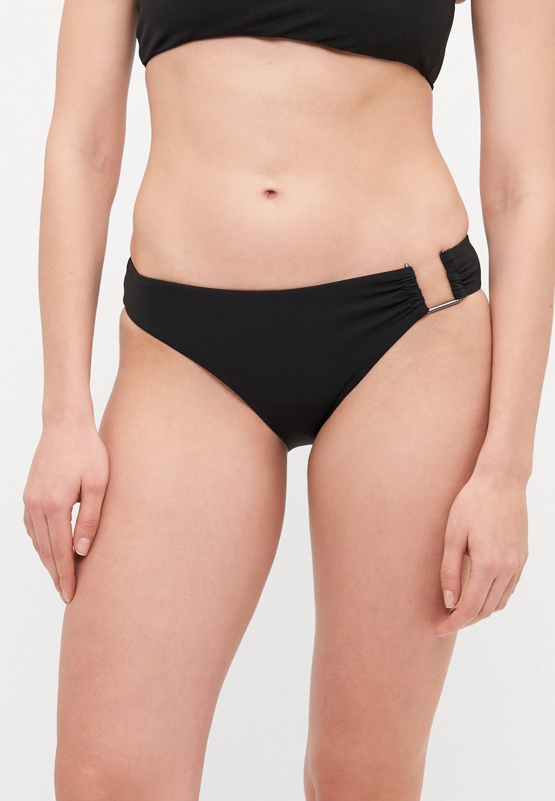 Juodas bikini apačios kelnaitės su šoniniu raukiniu ir metaliniu akcentu. Pagamintos iš lygaus audinio, su vidutiniu pjūviu ir be siūlių apdaila.