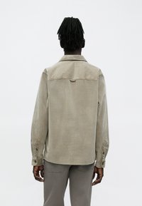 Lichtgrijs ribfluwelen jasje met een rugstuk, knoopmanchetten en een losse pasvorm. Heeft een gestructureerde stof en gedetailleerde stiksels.